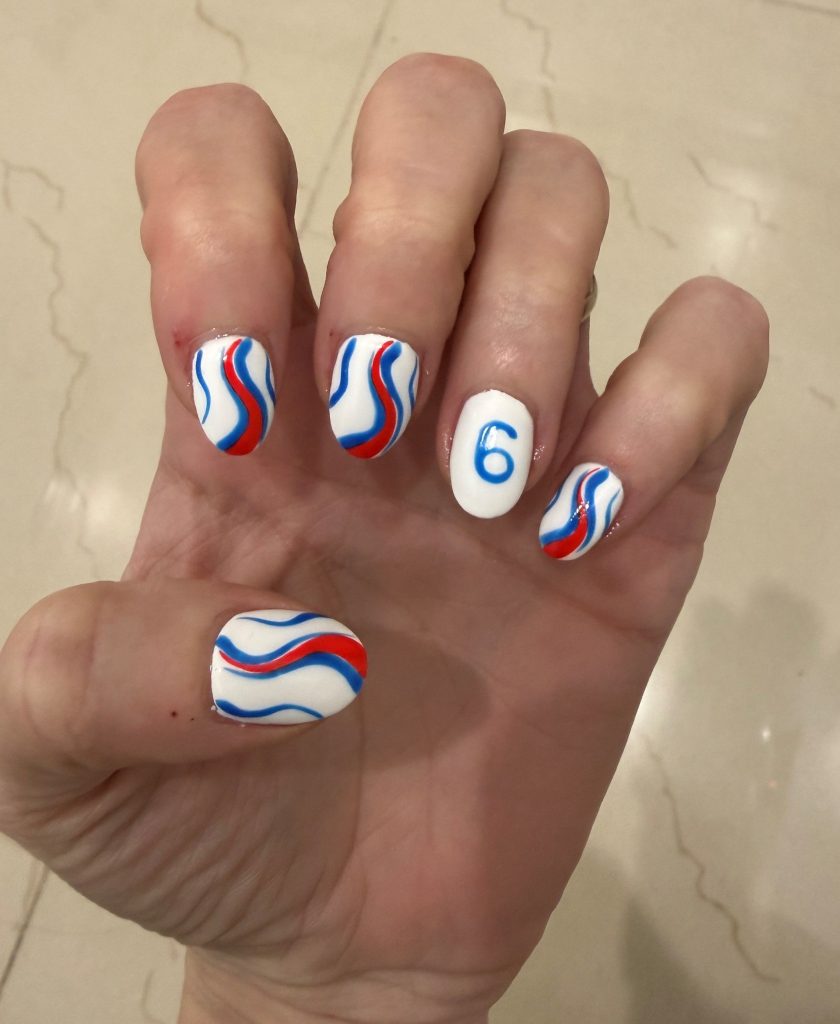 A hand displaying manicured nails with a design featuring white polish, blue and red wavy patterns, and the number '6' on one nail.