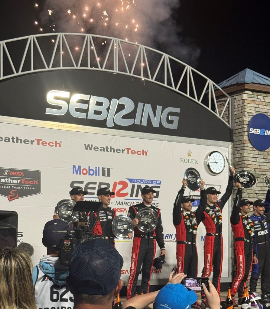 Celebration at the Sebring International Raceway with drivers holding trophies after a race, fireworks in the background.